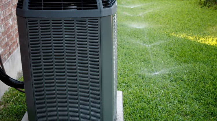 Modern air conditioner on backyard with working sprinkler system
