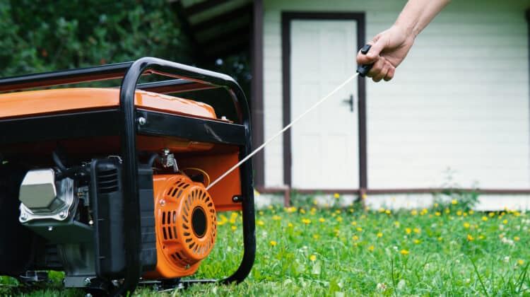 Hand starts a portable electric generator in front of a summer house in summer