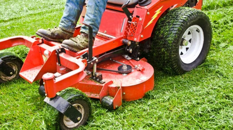 Man on a riding lawn mower that has grass stuck to the wheels