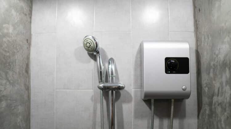 Instant tankless electric water heater installed on grey tile wall with input and output pipe/outlet and elcb safety breaker system and silver shower