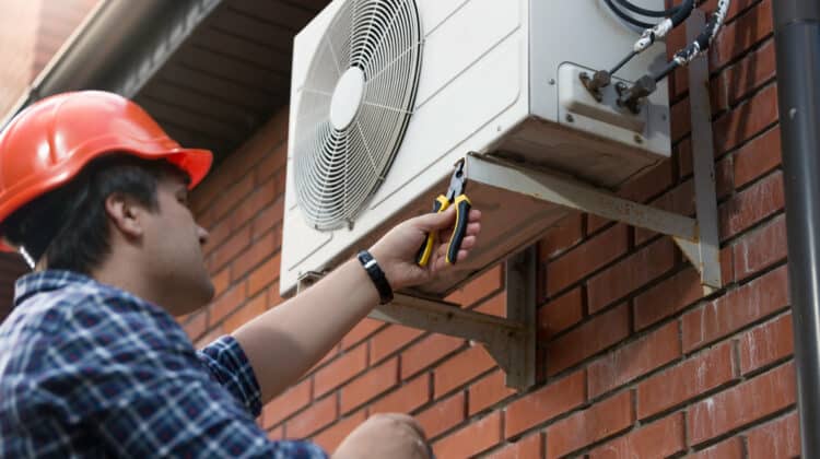 Portrait of young male technician in hardhat connecting air conditioning unit outdoor