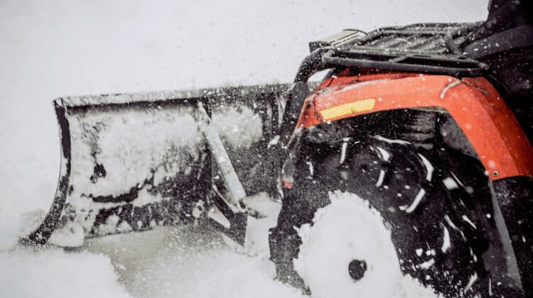 Truck with snow blade plowing atv quad bulldozer during storm on city road