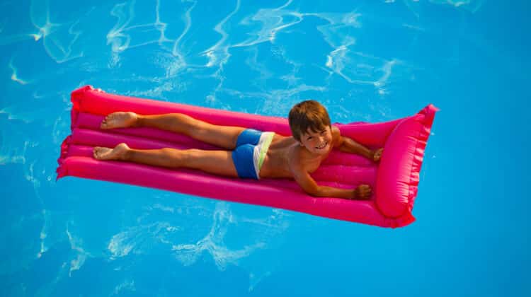 Happy smiling boy in pink swimsuit with inflatable mattress sunbathing on the beach at sunset