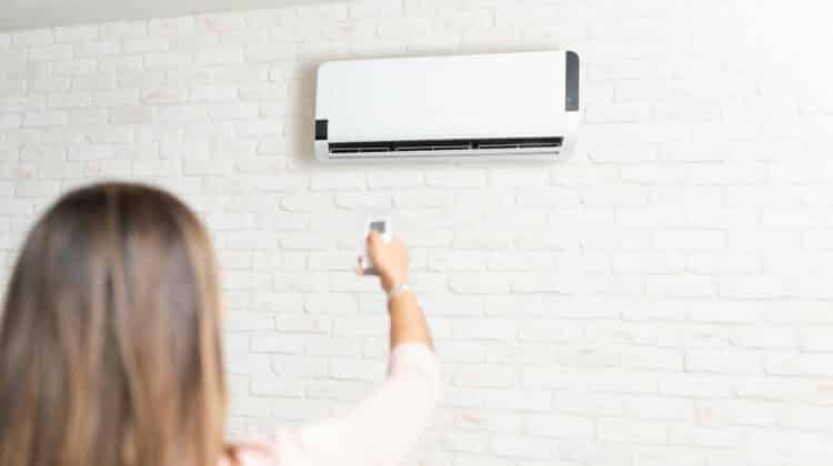 Side view of young latin woman adjusting air conditioner temperature with remote control at home