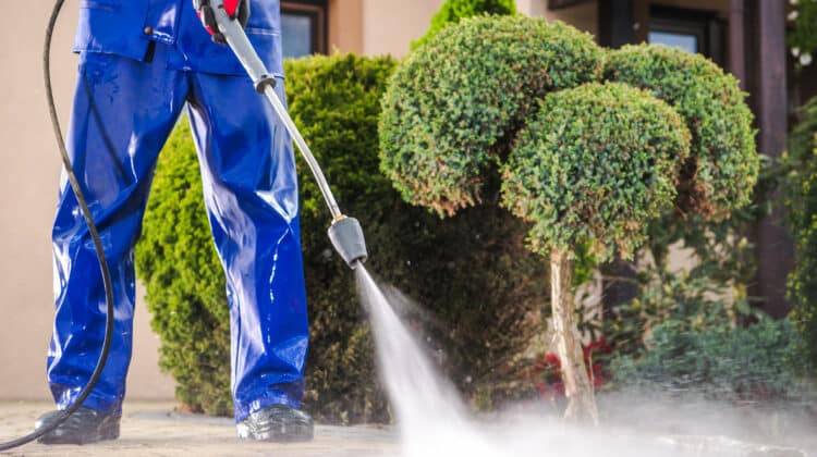 Worker using pressure water detergent cleaning home driveway with electric watering system