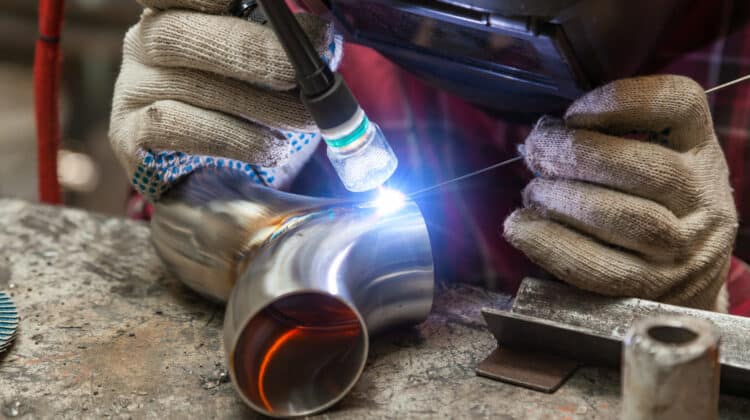 Young guy welder in a checkered red shirt welds a stainless steel