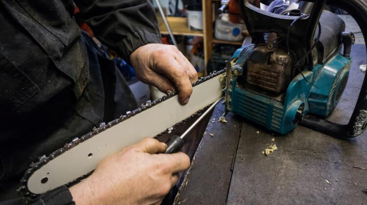 Man is cleaning the blade of a chainsaw from sawdust on a work bench in a mechanic shop