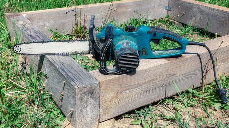 A large electric chainsaw lies on a wooden plank
