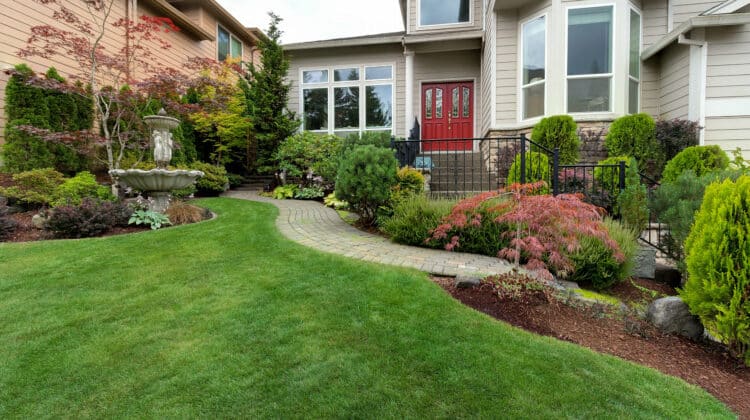 Outdoor landscaping of brick home with green lawn shrubs and grass paver and fountain