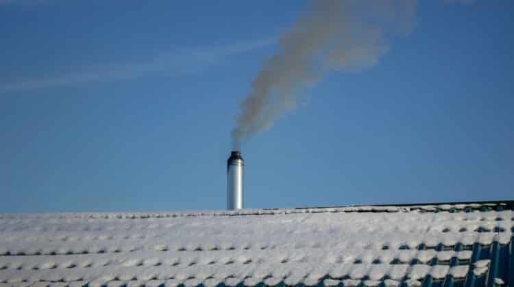 Modern steel chimney of a Russian sauna covered with snow against a blue sky