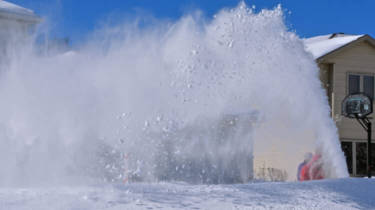 A snowblowers shoots out a cloud of snow while clearing driveway after a blizzard