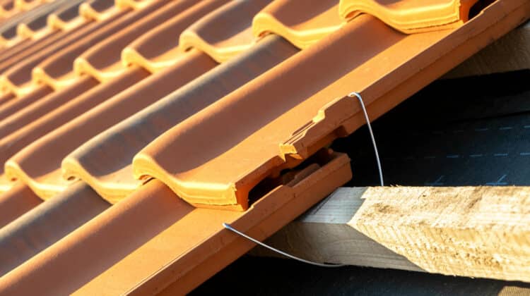 Closeup of metal montage anchor for installation of yellow ceramic roofing tiles mounted on wooden boards covering residential building roof under construction