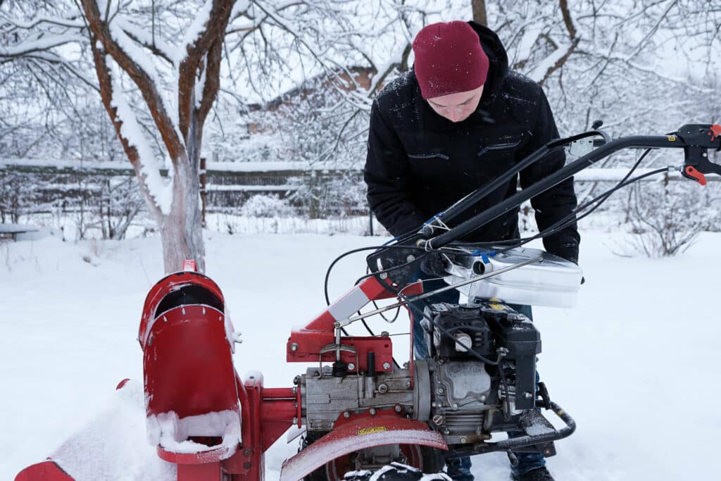a man pours gasoline from a canister into a snow blower tank