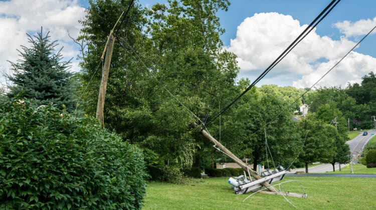 Broken snapped wooden power line post with electrical components on the ground after a storm