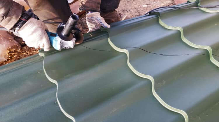 Professional electric engineering master cuts metal sheet into circles on roof of house in construction site