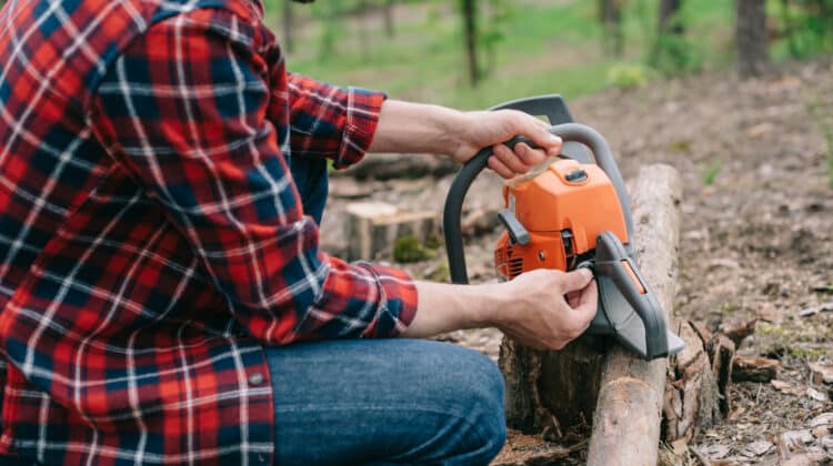 cropped view of lumberjack in plaid shirt repairing chainsaw in forest