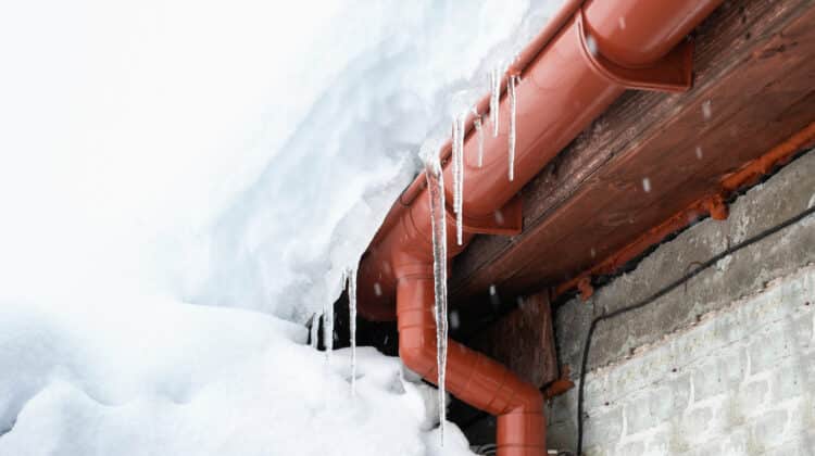A snowdrift on the roof of a house from which icicles hang Cleaning roofs from accumulated snow
