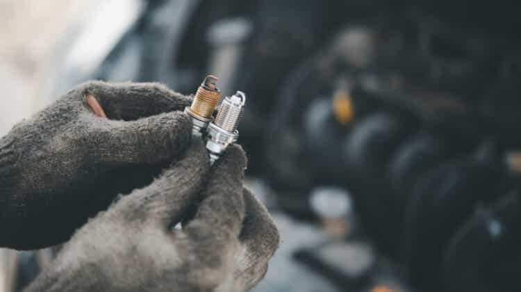 Spark plug replacement work Hand of the auto mechanic holding the old spark plug on blurred engine car on background