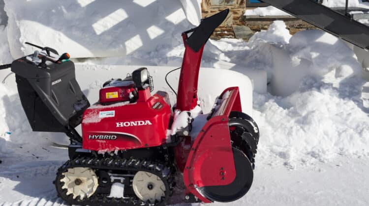 Petrol snow blower Honda on the track next to a snowdrift Sunny winter day red unit on the background of white fluffy snow
