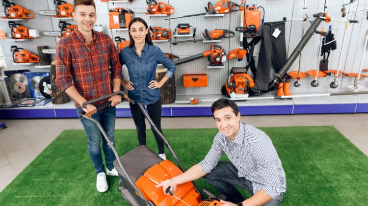 A consultant in a garden tools store shows a guy and a girl a lawn mower
