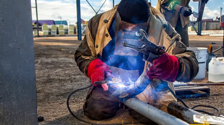 A strong man is a welder in brown uniform welding mask and welders leathers a metal product is welded with a arc welding machine at the construction site