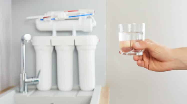 Mens hand holds a glass of clear water Tap and reverse osmosis filter in the background