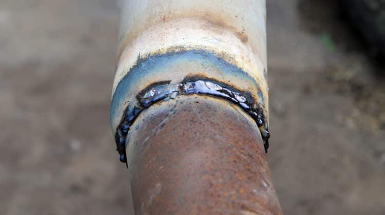 Rusty brown metal pipe and white painted one welded together