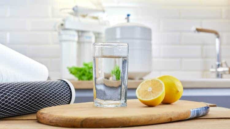 Glass of filtered clean water with reverse osmosis filter lemons and cartridges on table in kitchen Concept Household filtration or purification system.