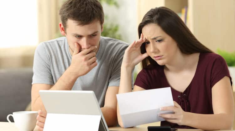 Worried couple reading together a letter sitting in a desk at home