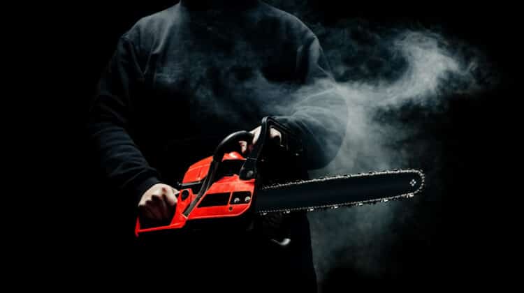 A man with a chainsaw in his hands close up against the background of smoke