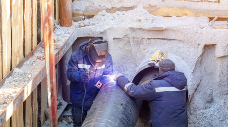 Repair and renewal of the city Assistant welder in protective gloves welds new utilitite trench