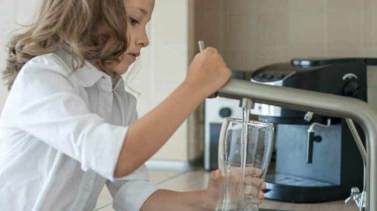 Portrait of a little caucasian girl gaining a glass of tap clean water. Kitchen faucet