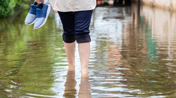 Woman holds her feet at road in flood water