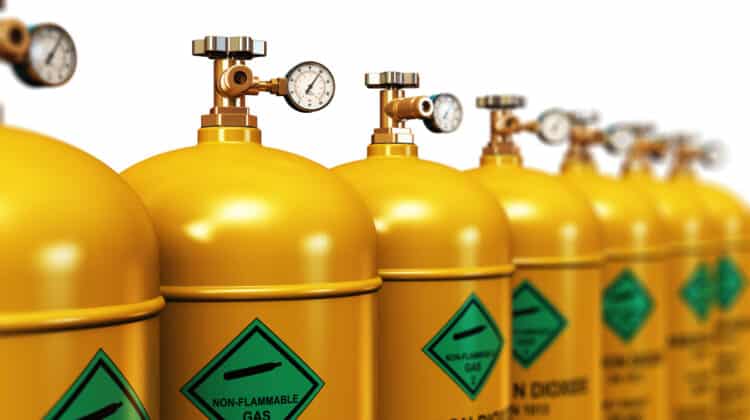 group of yellow metal steel liquefied compressed natural carbon dioxide gas containers or cylinders with high pressure gauge meters and valves arranged in row an