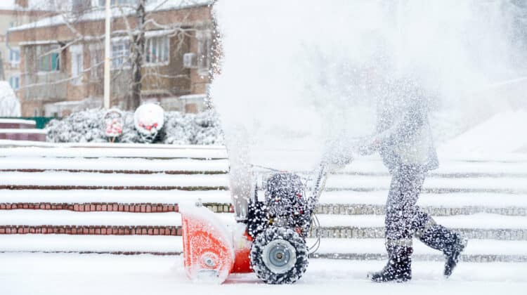 Man in orange clothes using snow blower for removing snow from frozen area