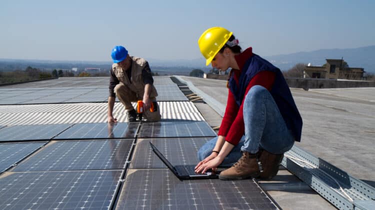Elderly woman in helmet working on photovoltaic panel at plant