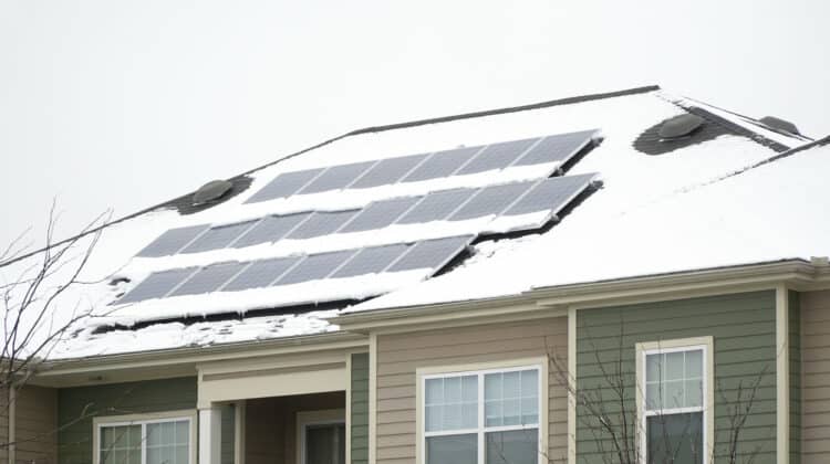 Solar panel on the roof of a house covered with snow and blue ice