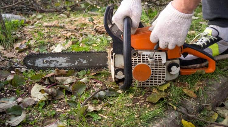 a man's hands start a chainsaw in the garden