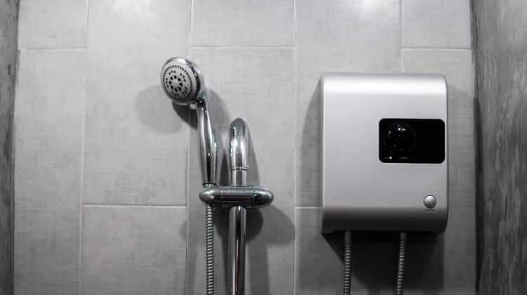 Silver tankless boiler with electric water output for hot bath on grey tiled background