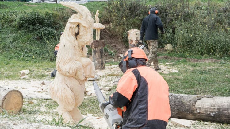 Master in special suit and headphone creating sculpture with chainsaw sawing wooden sheep