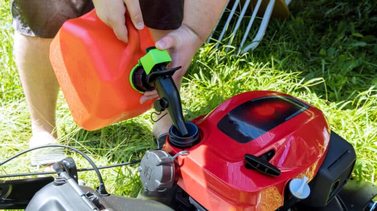 Pouring gasoline gallon refueling into the tank of lawn mower