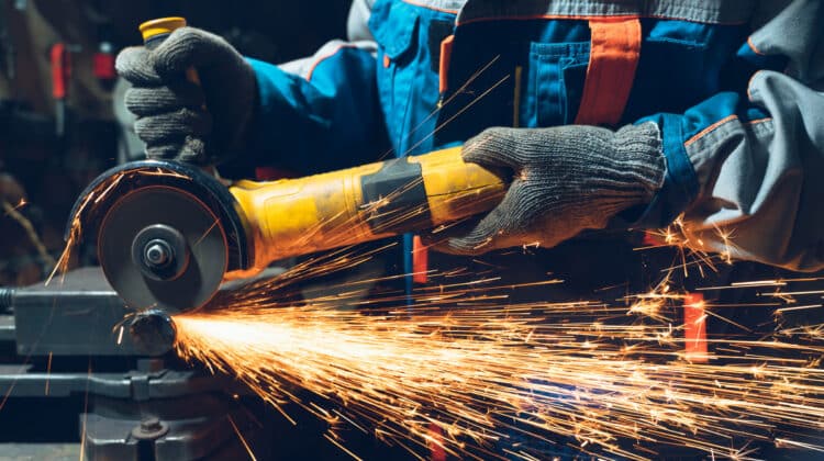 Human hand in work clothes goggles holding metal grinder Hot flame and sparks at high angle
