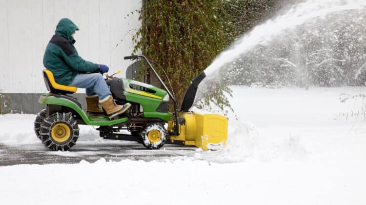 man on riding snow blower clearing snow out of residential driveway