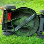 dirty electric lawn mower in green grass at home backyard