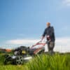 Man mowing cutting grass on his huge garden yard, green field by motor garden mower