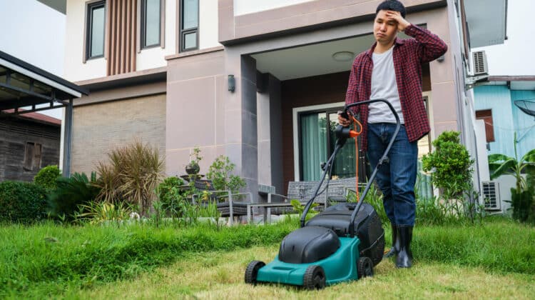 tired man using a lawn mower cutting grass at home