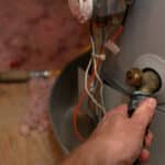 Hand attaches hose to water heater drain to perform maintenance